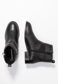 Botines negros de piel texturizada, con cremallera lateral, tacón bajo y una pestaña en la parte trasera para facilitar su uso.