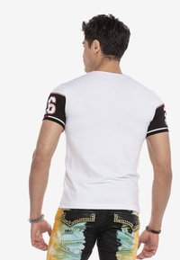 Witte t-shirt met korte mouwen en zwarte mouwen, met een rood nummer '36'. Gekleed met multicolour versleten jeans met gestanste accenten.