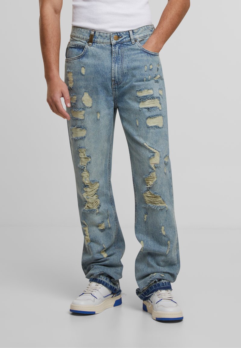 Jeans decolorate de un albastru deschis, cu găuri și margini tocite. Stil clasic cu cinci buzunare, cu închidere cu nasture și croială dreptă.
