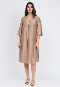 Vestido marrón claro hecho de una tela suave, con escote en V, mangas de tres cuartos y aberturas laterales para mayor comodidad de movimiento.