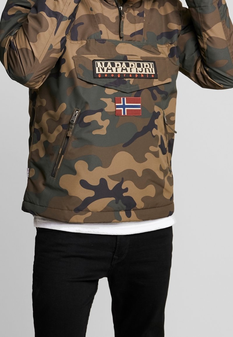 Chaqueta con capucha de patrón de camuflaje en tonos terrosos, que incluye un bolsillo con cremallera, parche con logo y acento de la bandera de Noruega. Textura suave.