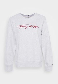 Světle šedá mikina s žebrovanými manžetami a lemem. Na hrudi je červený kurzívní nápis "Tommy Hilfiger". Hladký materiál ze směsi bavlny.