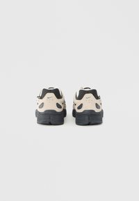 Το παπούτσι διαθέτει μπεζ επάνω μέρος με μαύρες λεπτομέρειες, υφασμένο γκρι πέλμα και χαρακτηριστικές μεγάλες εγκοπές στη φτέρνα. Το λογότυπο της Nike σε κάθε πλευρά.