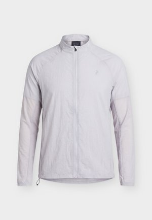 Veste zippée gris clair avec manches longues, col montant et logo discret sur la poitrine, présentée sur un fond uni.