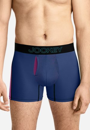 Männlicher Oberkörper trägt marineblaue und violette Boxershorts mit perforiertem Frontpanel und schwarzem Bund mit der Aufschrift Jockey.