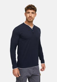 Navy long-sleeve henley shirt with white collar and accent, featuring three buttons at the neck and a fitted design. Soft cotton material.