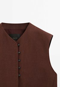 Veste marron sans manches avec col rond et six boutons noirs sur le devant, tissu texturé et fond uni.