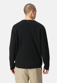 Suéter negro de punto con cuello redondo, mangas largas y corte relajado. La parte posterior presenta un pequeño detalle bordado en el escote. Textura suave.