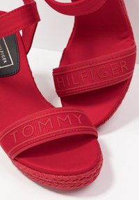 Sandales à plateforme rouges avec brides en tissu. Présentent les inscriptions en relief "TOMMY" et "HILFIGER" sur les brides, avec un détail de semelle tissée.