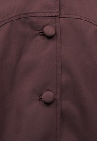 Κοντινό πλάνο βυσσινί υφάσματος με δύο κουμπιά καλυμμένα με το ίδιο ύφασμα, ραμμένα σε κάθετη ραφή με διακοσμητική διπλή ραφή сверху.