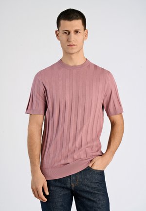 Lichtroze gebreide trui met korte mouwen, verticaal ribbelpatroon en ronde hals, gecombineerd met donkerdenim jeans.