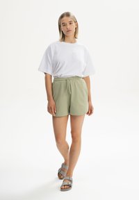 Wit T-shirt met korte mouwen, lichtgroene korte broek met elastische taille, grijze sandalen. Eenvoudig ontwerp, zacht stof, losse pasvorm, neutrale kleuren.