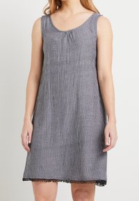 Ärmlös klänning i grått med vertikala vita ränder, rund halsringning och svart spetsdetalj vid fållen. Tillverkad av lättviktig tyg.