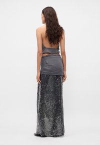 Top de satén gris con la espalda descubierta, combinado con una falda larga de lentejuelas en tonos plateados. La tela texturizada crea un efecto brillante.