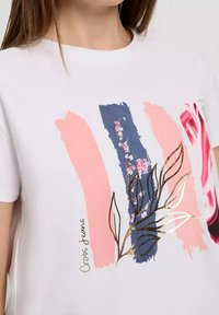 Biała koszulka z różowymi i niebieskimi wzorami malarskimi, florystycznymi grafikami oraz liśćmi z złotymi akcentami. Logo "Cross Jeans" nadrukowane z boku.