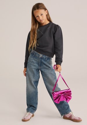 Sweatshirt noir avec détails cloutés, jean en denim bleu clair et un sac à main rose brillant avec un accent en nœud. Baskets dans une teinte pâle.