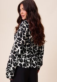 Czarna i biała bluzka z kwiatowym wzorem, długimi rękawami, marszczonym pasem i gładkim, lekkim materiałem.