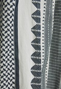 Tissu présentant des motifs géométriques alternés en bleu marine et blanc, incluant des zigzags et des hexagones, avec une texture lisse.