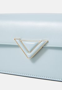 Borsa a tracolla in pelle blu chiaro con un accento geometrico dorato, caratterizzata da una superficie liscia e cuciture precise lungo i bordi.