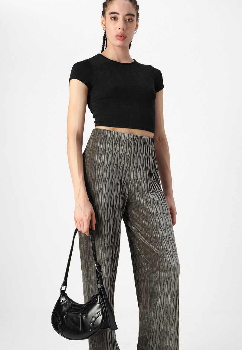 Schwarzes, kurzes T-Shirt, kombiniert mit silbernen, gefältelten, weiten Hosen und einer kleinen schwarzen Lederhandtasche mit abgerundeten Akzenten und einem Schulterriemen.
