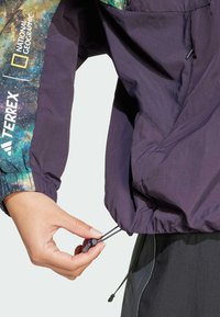 Purple lightweight jacket with elastic cuffs and adjustable hem. Features a colorful galaxy-patterned panel on the hood.