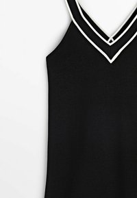 Top nero senza maniche con scollatura a V caratterizzato da bordi bianchi. Il tessuto è a costine, aggiungendo texture all'aspetto complessivo.
