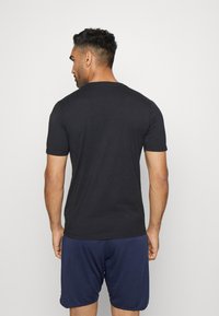 Zwarte katoenen t-shirt met korte mouwen, voorzien van een ronde hals en een slim fit ontwerp. Draagt met marineblauwe shorts.