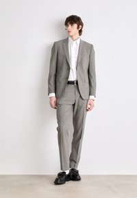 Completo grigio a quadri con giacca aderente e pantaloni abbinati. Indossato sopra una camicia bianca, abbinato a una cintura nera e scarpe nere di grosse dimensioni.