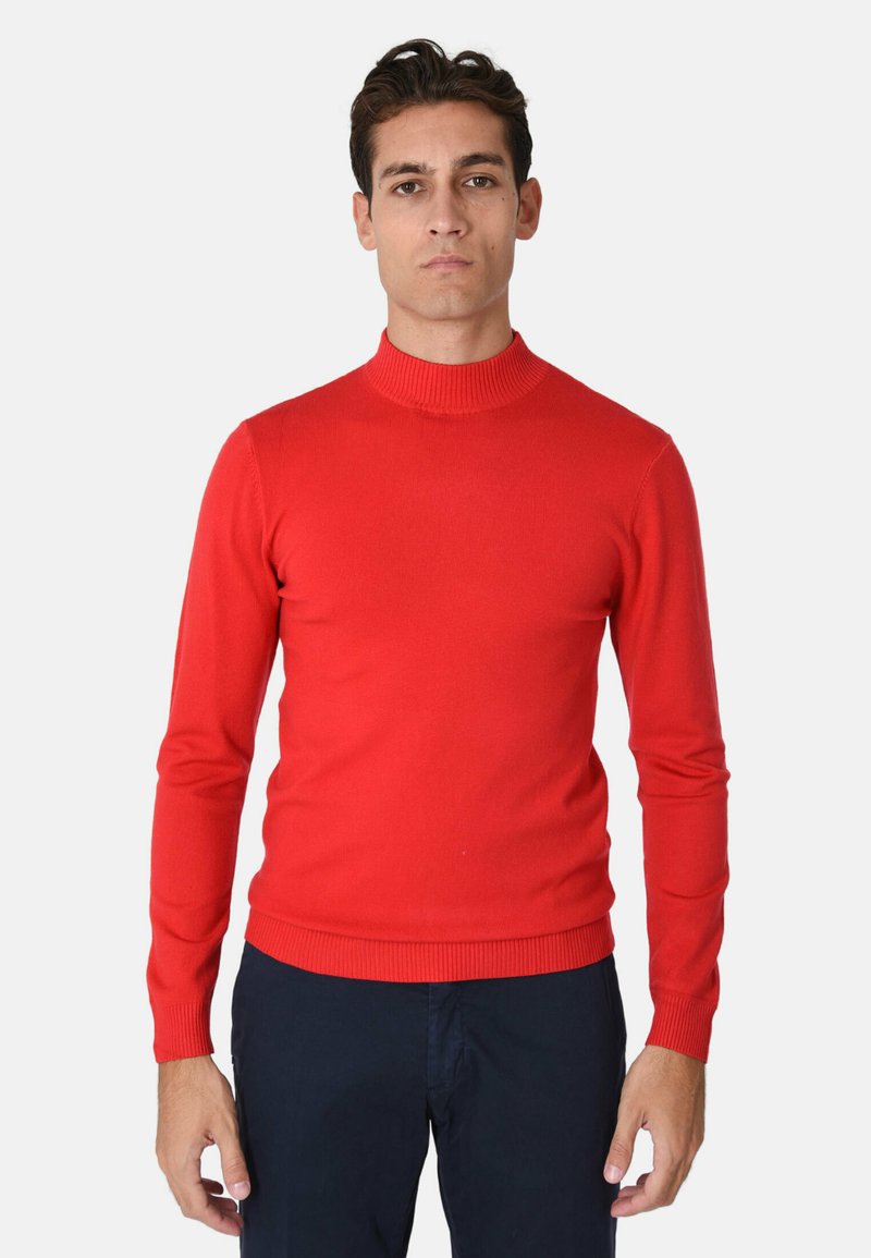 Maglione rosso a maniche lunghe con collo alto a costine. Texture liscia e design aderente. Abbinato a pantaloni scuri, indossato da una modella.