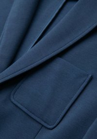 Närbild av en marinblå blazerficka och slag som visar textilstruktur och detaljerad sömnad.