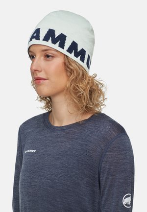 Light blue knit beanie with bold navy "MAMMUT" logo. Worn with a dark blue long-sleeve shirt featuring a small logo on the sleeve.