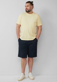 Gele katoenen T-shirt, marineblauwe shorts, witte sneakers. Relaxte pasvorm; casual stijl met korte mouwen en zakken. Eenvoudig ontwerp, geen patronen.