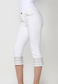 Jean blanc cropped avec un design ajusté, des ourlets effilochés et des accents texturés autour des poignets pour plus de détails.