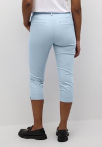 Blue cropped pants with a textured fabric, featuring a back yoke and two rear pockets. Paired with black loafers for contrast.