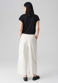 Top nero a maniche corte abbinato a pantaloni beige chiaro a vita alta e dal taglio morbido. Design semplice senza pattern o decorazioni visibili.