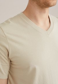 V veida kakla T-kreklā gaiši beidzēta kokvilna, īsas piedurknes, pieguļošs piegriezums, gluda tekstūra, ar smalkiem šuvju detaļām.