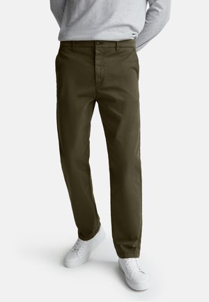 Donkergroene broek van katoen met een flat front, zijzakken en een knoopsluiting, gecombineerd met witte sneakers.
