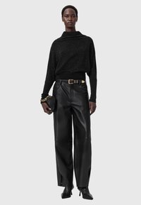 Schwarzer glitzernder Pullover mit hohem Kragen, kombiniert mit schwarzen weit geschnittenen Lederhosen, einem goldenen Gürtel und einer kleinen Clutch-Handtasche.