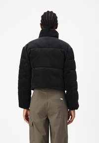 Sort corduroy cropped puffer-jakke med høj krave og ribbet tekstur. Sammen med olivengrønne bukser med en baglomme.