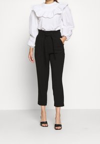 Vit blus med volangkrage och puffärmar, parat med svart byxor med hög midja. Slim fit, ankellängd och detalj med knytbälte.