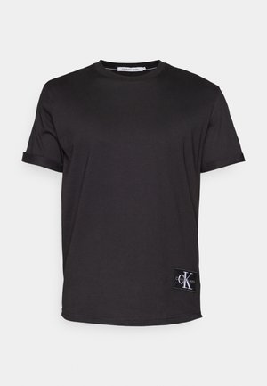 Musta puuvillainen t-paita lyhyillä hihoilla, pyöreällä kaula-aukolla ja pienellä Calvin Klein Jeans -tunnuksella alhaalla vasemmalla puolella. Sileä rakenne.