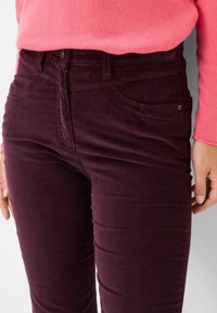 Bordeaux corduroy broek met een gladde textuur, voorzien van vijf zakken en een slim fit ontwerp, gecombineerd met een roze trui bij de taille.