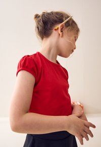 Red cotton T-shirt with short puff sleeves and a round neckline, worn with a dark skirt. A pencil is tucked behind the ear.