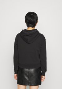 Sudadera negra recortada con capucha ajustable, puños acanalados y una banda con logo en el cuello, combinada con una minifalda de cuero negra.