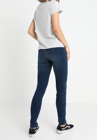 Jeans ajustados de mezclilla azul oscuro, con una cintura de altura media y costuras sutiles. Combinados con una camiseta de manga corta gris claro y zapatillas negras.