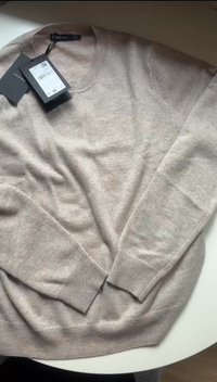 Beige kashmir neule, jossa on V-henkinen muotoilu, pitkät hihat ja ribbireunukset. Kaulaan kiinnitetyt tarrat tarjoavat lisätietoja tuotteesta.