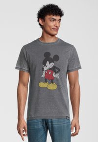 Šedé bavlněné tričko s velkým černým a červeným grafickým motivem Mickey Mouse, kulatým výstřihem a krátkými rukávy. Doplňuje ho žluté boty.