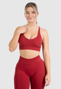 Rode sportbeha met een diepe hals en brede schouderbanden, gecombineerd met hoge taille leggings, beide gemaakt van een gladde, rekbare stof.