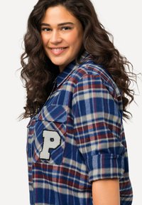 Blauw, rood en beige geruite flanellen shirt met lange mouwen, een borstzak met een witte "P" patch en opgerolde mouwen.