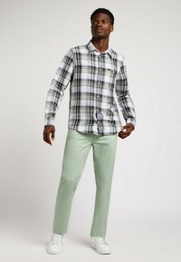 Koszula w kratę w białym, czarnym i zielonym kolorze, zestawiona z miętowymi spodniami i białymi sneakersami. Strój charakteryzuje się luźnym krojem.